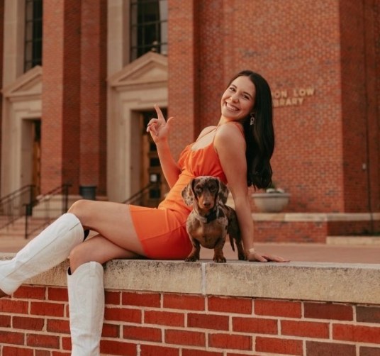 Kimberlyn Russell, owner of The Daily Paw, sitting on a brick wall with a dachshund